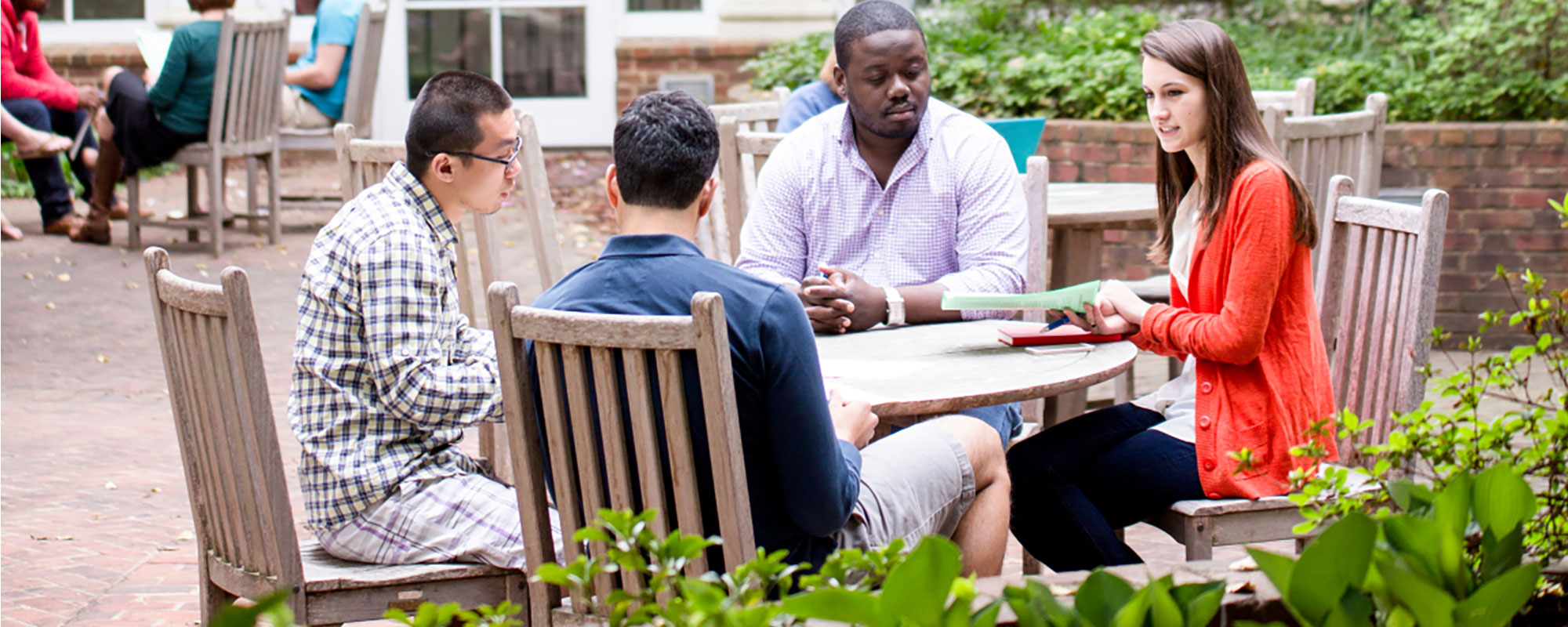 Four students meeting at table on Newcomb Hall outdoor patio