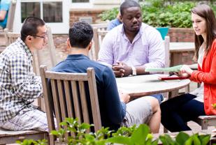 Four students meeting at table on Newcomb Hall outdoor patio